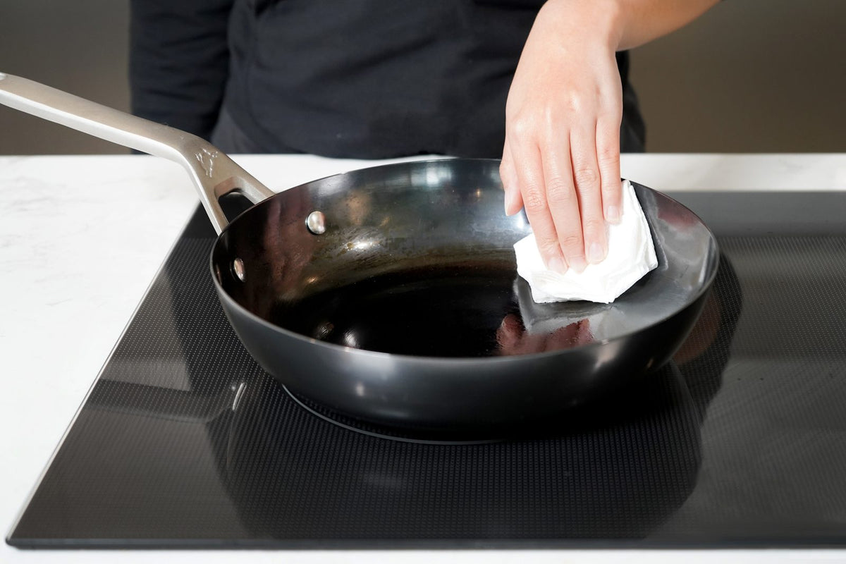 Person wiping the inside of a carbon steel pan after cooking