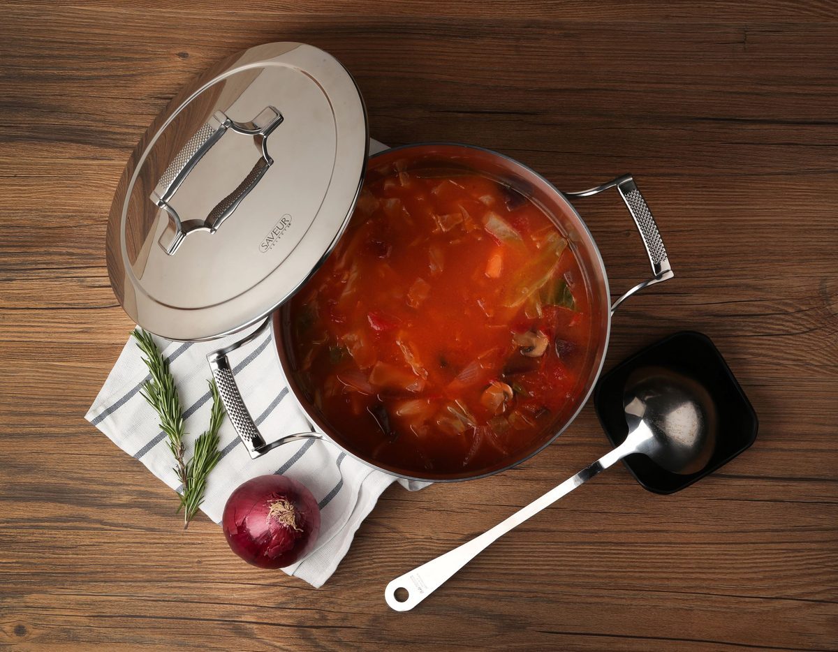Stainless steel stockpot filled with soup on a wooden kitchen surface