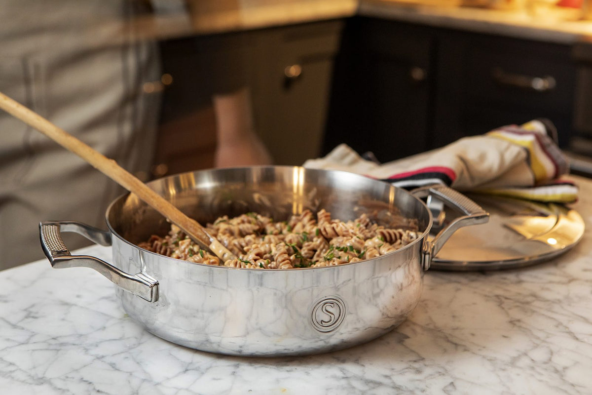 A stainless steel sauté pan being used for a one-pan meal in a home kitchen