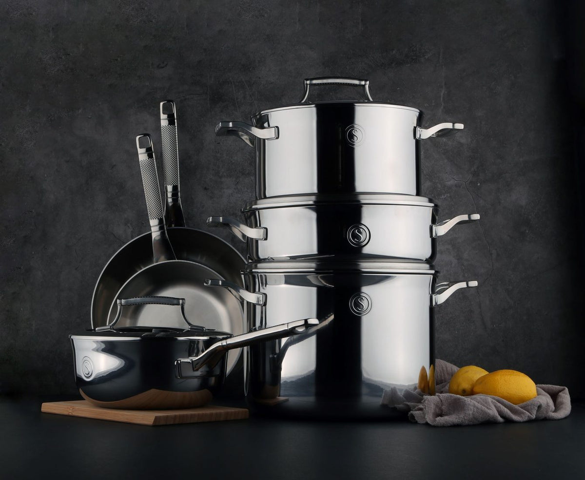 Tri-ply stainless steel cookware arranged on a kitchen worktop